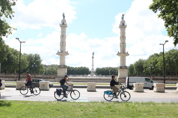 Trois cyclistes et une personne en roller sur la piste cyclable devant la place des Quinconces, à Bordeaux.