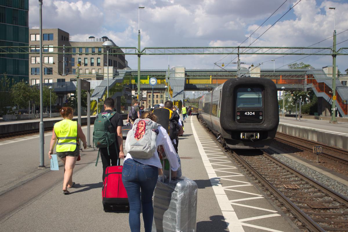 Des étudiants font rouler leur valise sur le quai de la gare de Lund, vers l'ascenseur. Le train Öresundståg part lui dans la même direction, vers Hassleholm.
