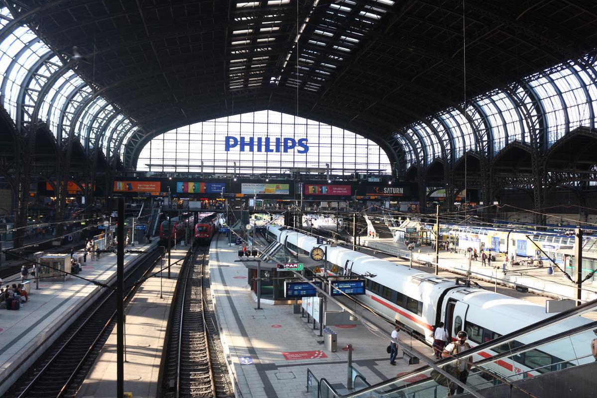 Gare d'Hambourg, Allemagne. Une immense verrière sombre protège les trains. Au fond, un grand logo PHILIPS, qui sponsorise la gare ?
